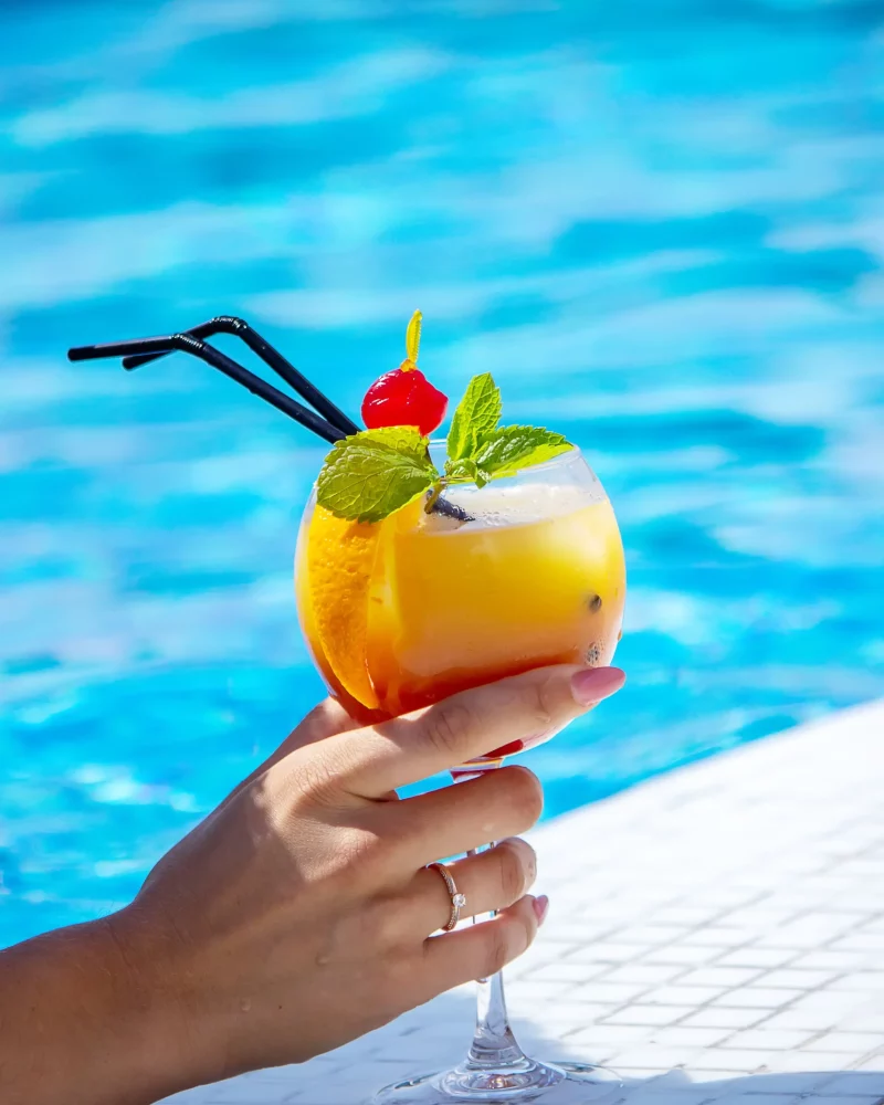 young-woman-is-resting-pool-drinks-cocktail-with-freshly-squeezed-orange